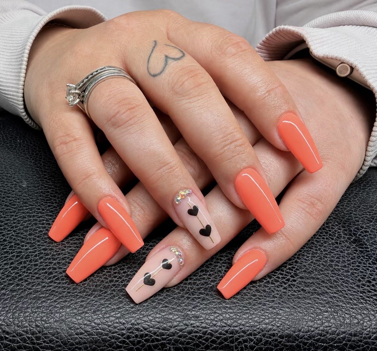 Coffin nagels in koraaloranje met een nude accentnagel met zwarte hartjes en steentjes